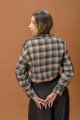 Camisa de manga larga con diseño a cuadros en tonos grises, marrones y ocres. Presenta cuello clásico, cierre frontal con botones, un bolsillo frontal y parches en los codos en contraste de color marrón.