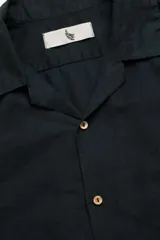 Camisa negra de manga corta con cuello camp y calce relajado. Confeccionada en mezcla de algodón y lino con botones de coco con logo y parche característico de Polonio.