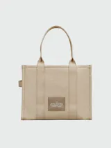Bolso tipo tote de gran tamaño en color beige, confeccionado en lona resistente. Presenta el logo distintivo de la marca estampado en la parte frontal con letras blancas. Cuenta con doble asa superior para llevar al hombro y cierre superior con cremallera.