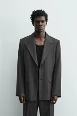 Blazer de corte regular fit en color gris oscuro, confeccionada en tejido con viscosa. Presenta cuello con solapas de muesca, cierre frontal con dos botones, bolsillos laterales con solapa y aberturas en la espalda.