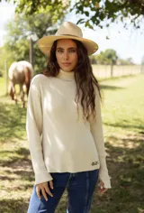 Polera de tejido de punto acanalado color beige, con cuello alto, manga larga y detalle de logo bordado en el ruedo.