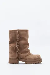 Bota de caña media con flecos laterales, confeccionada en material con textura tipo gamuza. Presenta una silueta relajada y suela robusta con base dentada.