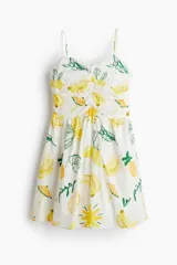 Vestido corto blanco con estampado de bananas, limones, piñas y sombrillas. Tiene breteles finos ajustables, escote corazón y cuerpo entallado con frunces en el escote y laterales. La falda es levemente acampanada.