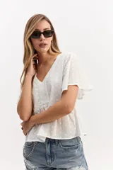 Blusa blanca de algodón con escote en V, mangas amplias y vuelo suave. Cuenta con un recorte en la cintura con frunce que aporta volumen y una caída fluida, además de una textura sutil con bordado inglés.