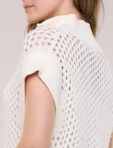 Buzo de punto color marfil, confeccionado en algodón calado con cuello alto acanalado y medio cierre metálico dorado. Presenta mangas cortas estilo japonesa con puños anchos y un zócalo acanalado en el ruedo.
