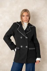 Blazer cruzado de paño color negro, con cierre de botones frontales. Presenta solapas con bordes decorados en contraste, bolsillos con solapa y un detalle de flor en la solapa, todo con acabados artesanales.