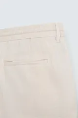 Bermuda de corte relajado color beige claro, confeccionada en lino. Presenta cintura elástica con cordón ajustable y bolsillos laterales y traseros.