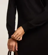 Vestido de punto negro, de manga larga y cuello alto, con corte recto y largo midi.