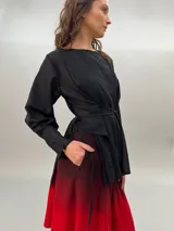 Blusa negra de lana y poliéster, liviana y sutilmente transparente, con terminación asimétrica y tablas que le brindan volumen y movimiento. Presenta dos lazos delanteros que permiten ajustar a gusto adelante y/o atrás.