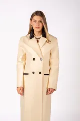 Tapado largo de paño color beige, con diseño de doble botonadura, solapas con detalle en contraste negro y bolsillos laterales con ribete negro.