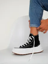 Championes tipo botita de caña alta con diseño bicolor, cuerpo en color negro y suela de plataforma gruesa en color blanco con base de goma.