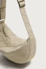 Bolso de hombro de nylon color negro, con diseño curvo y cierre de cremallera en el compartimento principal. Cuenta con asa ajustable para llevar al hombro y bolsillo interior con cierre.