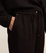 Pantalón de crepé rojo, modelo estilo pijama, de corte fluido, con cintura elástica y lazo de ajuste con terminales metálicas. Cuenta con bolsillos laterales y cierre frontal con cremallera y botón.