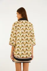 Camisa de algodón con estampado floral y de aves, cuello camisero oscuro y cierre frontal parcial con botones. Mangas amplias de largo codo con ribetes en contraste.