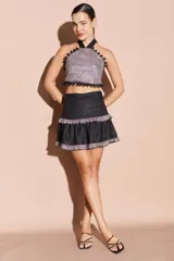 Top halter con acabado brillante, escote alto y detalles de ojalillos decorativos en los bordes. Diseño con espalda descubierta y cierre ajustable.