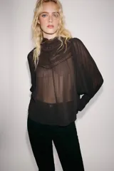 Blusa de cuello subido y manga larga, color marrón oscuro, con detalles de bordados combinados a tono en el canesú y los puños anchos. Cierre en la espalda con abertura y botones.