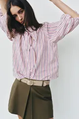 Camisa de rayas verticales rojas, blancas y azules, con cuello alto decorado con lazada, mangas abullonadas por debajo del codo y cierre frontal de botones forrados.