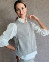 Chaleco de corte recto y largo a la cintura, confeccionado en denim con estampado de rayas verticales en tonos azul y blanco. Presenta cuello redondo y costuras visibles que definen su estructura.