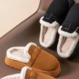 Pantuflas de gamuza color tostado, sin talón, con interior de corderito sintético, suela alta y tira decorativa con hebilla metálica en el empeine.