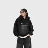 Hoodie negro de corte oversize con efecto desgastado, capucha y bolsillo frontal tipo canguro. Presenta estampado gráfico con texto en el pecho y detalle en la manga.