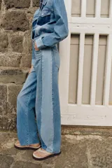 Jeans de tiro medio con diseño barrel y paneles laterales en un tono de denim más claro que contrasta con el centro. Presenta cinco bolsillos, cierre frontal con cremallera y botón, y bajo con acabado sin costura.