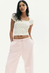 Remera corta de punto acanalado color crema, con estampado floral diminuto en tonos rosados y marrones. Presenta escote cuadrado con ribete de picot y mangas cortas ajustadas.