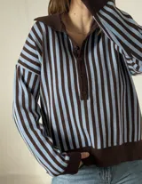 Sweater de punto a rayas verticales en color marrón y celeste, con cuello polo y cierre frontal de botones. Presenta mangas largas con puños ajustados y diseño holgado.