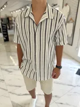 Camisa de manga corta de corte oversize en color blanco con rayas verticales negras, cuello camisero y cierre frontal con botones.