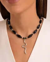 Collar de cristalitos facetados negros, con cuentas en forma de barril y rombos, y un dije colgante en forma de serpiente plateada de acero.