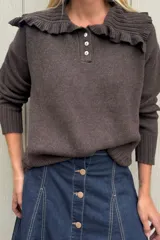 Sweater de punto color marrón, con cuello tipo babero con volados y cierre frontal parcial con tres botones. Presenta mangas largas con puños acanalados y diseño holgado.
