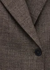 Blazer de corte recto y cruzado color marrón jaspeado, confeccionado en mezcla de lino. Presenta cuello pico con solapa de muesca, cierre delantero de un botón y dos bolsillos con solapa en los laterales.