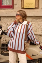 Buzo tejido de punto con diseño a rayas verticales en color celeste y marrón chocolate. Presenta un cuello polo con solapa en color crema y cierre frontal de tres botones, mangas largas de corte holgado y terminaciones en tejido acanalado.