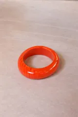 Pulsera rígida de resina con diseño orgánico y acabado brillante, disponible en colores marrón, gris y naranja.