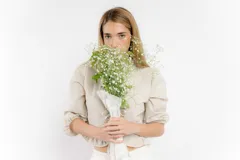 Blusa corta blanca de lino con mangas 3/4 abullonadas, escote en V con volados y cierre con lazos.