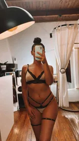 Conjunto de lencería de cuatro piezas compuesto por bralette, tanga, portaligas y ligas. Confeccionado en lycra beige con detalles de encaje negro en los bordes y tiras elásticas decorativas.