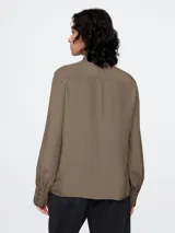 Blusa de satén color marrón topo, con cuello tipo lazo o moña, mangas largas con puños abotonados y corte fluido.