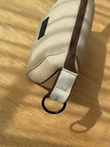 Neceser de neopreno color borgoña, con cierre superior y forro interior. Tiene un asa de mano con una franja azul y blanca.