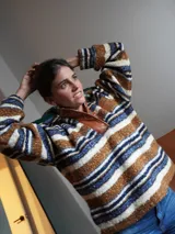 Buzo canguro oversize de paño de lana gris con capucha estampada y cuello de corderito blanco. Cuenta con aberturas laterales en el ruedo y detalles de cuero sintético marrón en el cierre frontal y etiqueta.