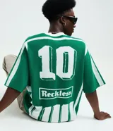 Remera de punto manga corta con diseño rayado vertical en color verde y blanco. Presenta cuello redondo, sisa desplazada y detalles gráficos tipo jersey de fútbol con el número 10 y el logo de la marca Reckless en el frente.