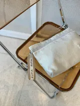 Sobre de mano color plateado con acabado texturizado y cierre superior. Incluye una correa de muñeca personalizada con la marca Rupia y detalles en yute.
