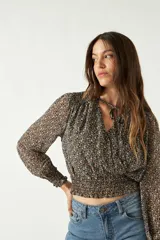 Blusa de manga larga con estampado floral pequeño sobre fondo oscuro. Presenta escote en V con lazo para anudar, cintura con frunce elástico y puños ajustados.