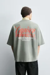 Sudadera de corte boxy fit, color verde oliva con efecto lavado. Presenta cuello redondo, manga corta terminada en rib y textos estampados a contraste en color rojo en el pecho.