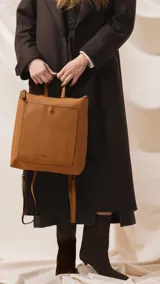 Mochila de diseño moderno y funcional, confeccionada en símil cuero con textura granulada. Cuenta con un bolsillo frontal con broche, cierre principal superior, manija superior y correas ajustables. Incluye logo de la marca grabado en el frente.
