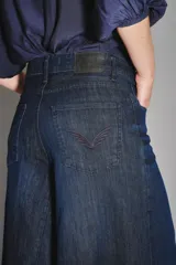 Pantalón de jean de tiro alto y pierna ultra ancha, confeccionado en denim confort con elastano y lavado azul oscuro. Presenta bolsillos traseros con bordado de alas y forrería estampada con el logo de la marca.