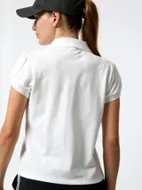 Remera polo de piqué color blanco, con manga corta abullonada, escote en V profundo y cuello clásico.
