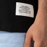 Remera oversize de lino entramado color blanco off-white, con cuello redondo, mangas cortas de hombro caído y etiqueta aplicada en el borde inferior.