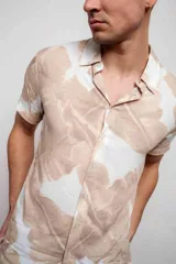 Camisa de manga corta con estampado de hojas en tonos beige y blanco, con cuello clásico y cierre frontal con botones.