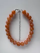 Collar de cuentas esféricas grandes con efecto marmolado en tonos anaranjados y salmón, con cadena de extensión y cierre metálicos.