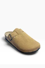 Zueco de gamuza color tostado, con diseño cerrado en la parte delantera y tira ajustable con hebilla metálica en el empeine. Cuenta con suela de corcho y base de goma antideslizante.