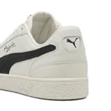 Championes urbanos Puma modelo Majesty, color beige con franja lateral característica en negro y detalle de firma en el lateral. Presenta suela de goma con textura y perforaciones en la puntera para mayor ventilación.